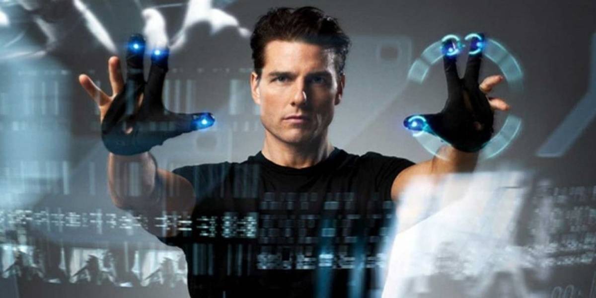 Tom Cruise vestindo uma camiseta preta, com as mãos estendidas em direção a uma tela no filme Minority Report