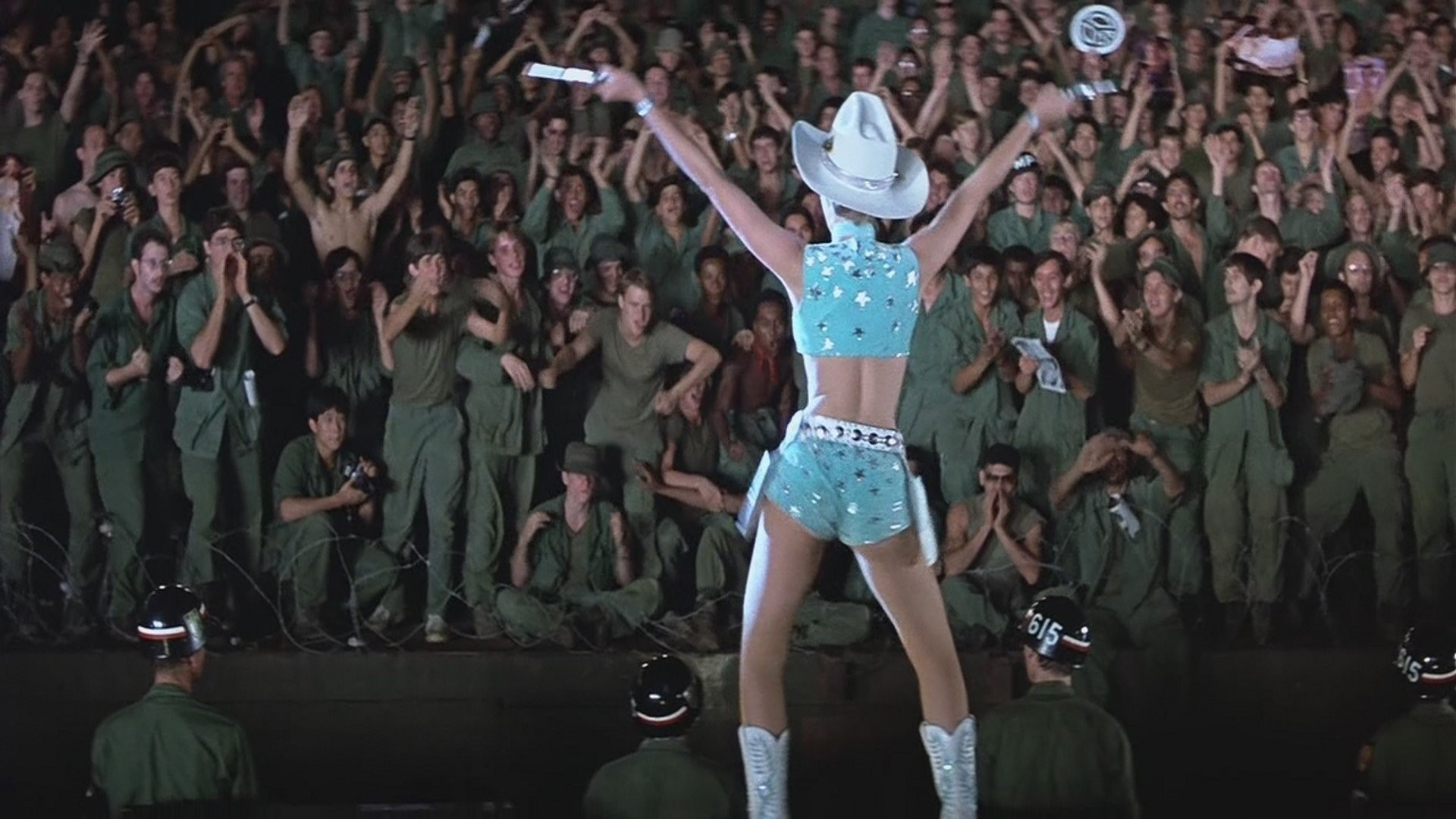 Mulher dançando em palco de cassino para multidão de soldados em uniforme verde durante apresentação militar noturna