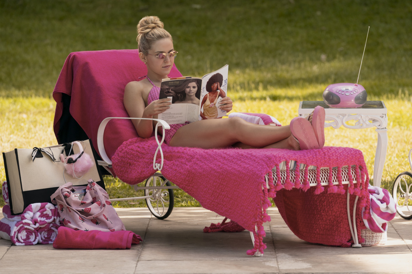 Atriz loira em look escolar com detalhes rosados, pose descontraída em cenário outdoor com iluminação natural