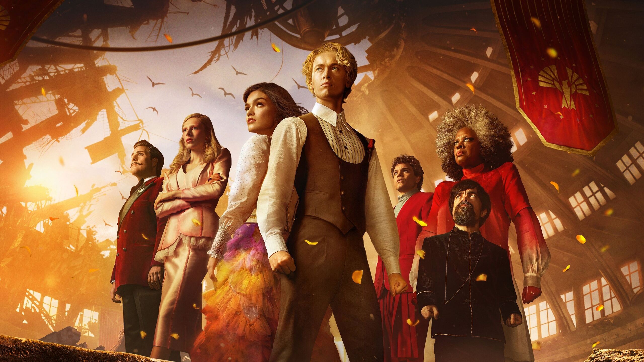 Elenco de prequel em formação reunida com personagem central de colete branco entre figuras coloridas em ambiente dourado com pétalas voando