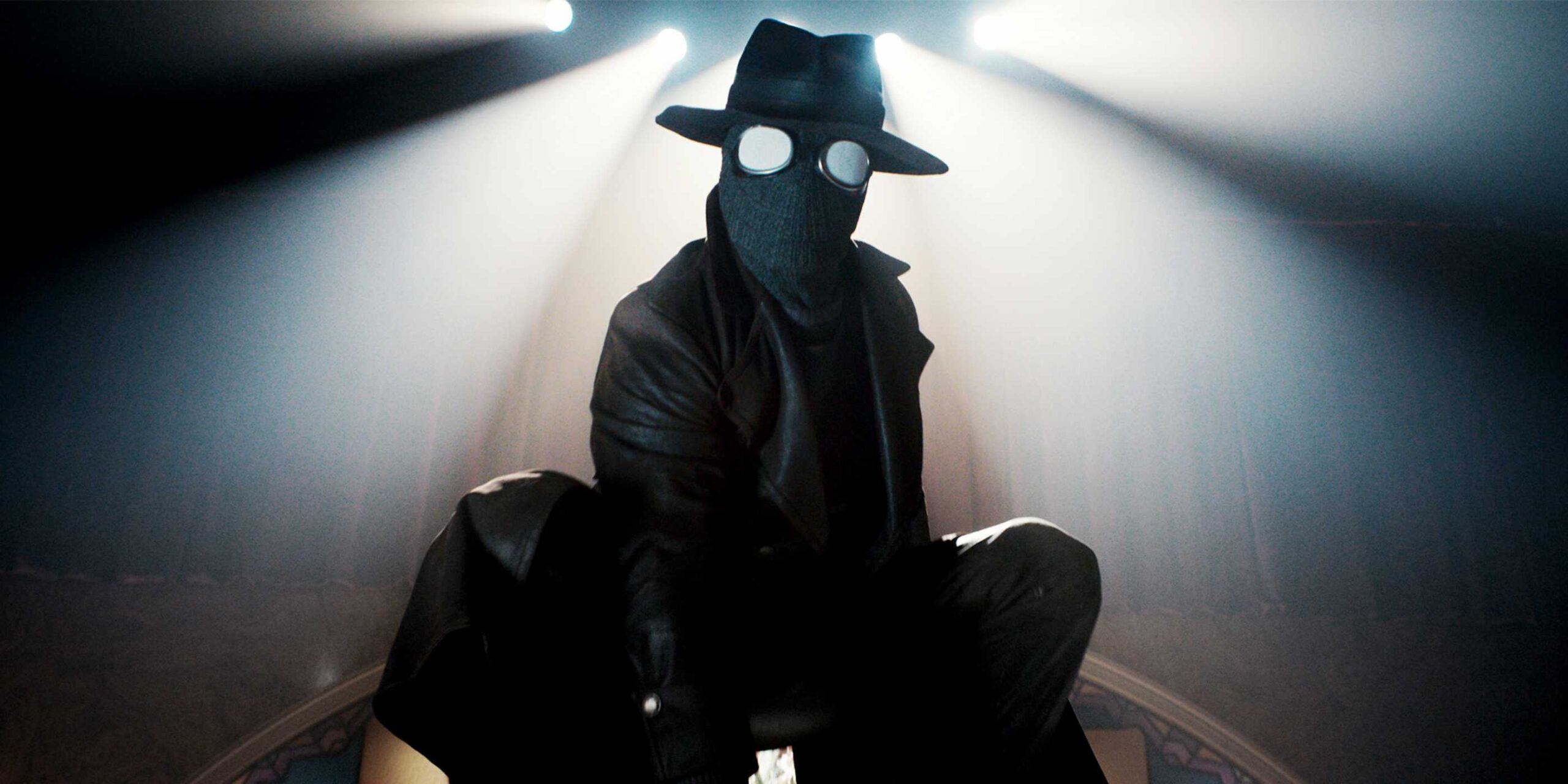 Nicolas Cage como The Spider agachado em uma mesa com a fantasia em Spider-Noir