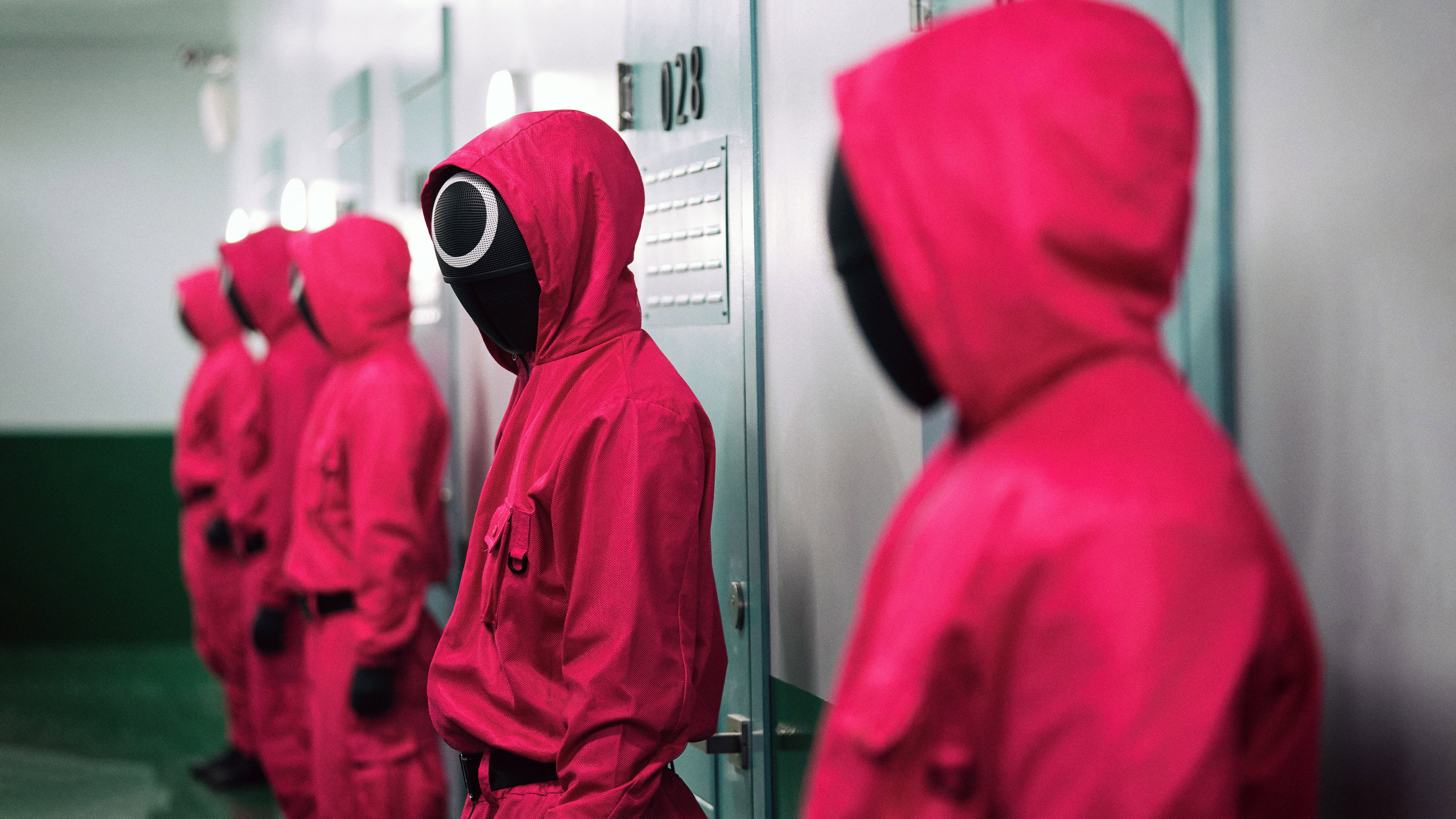 Guardas em uniformes rosa fluorescente com capuz e máscaras pretas com símbolos geométricos brancos em fila