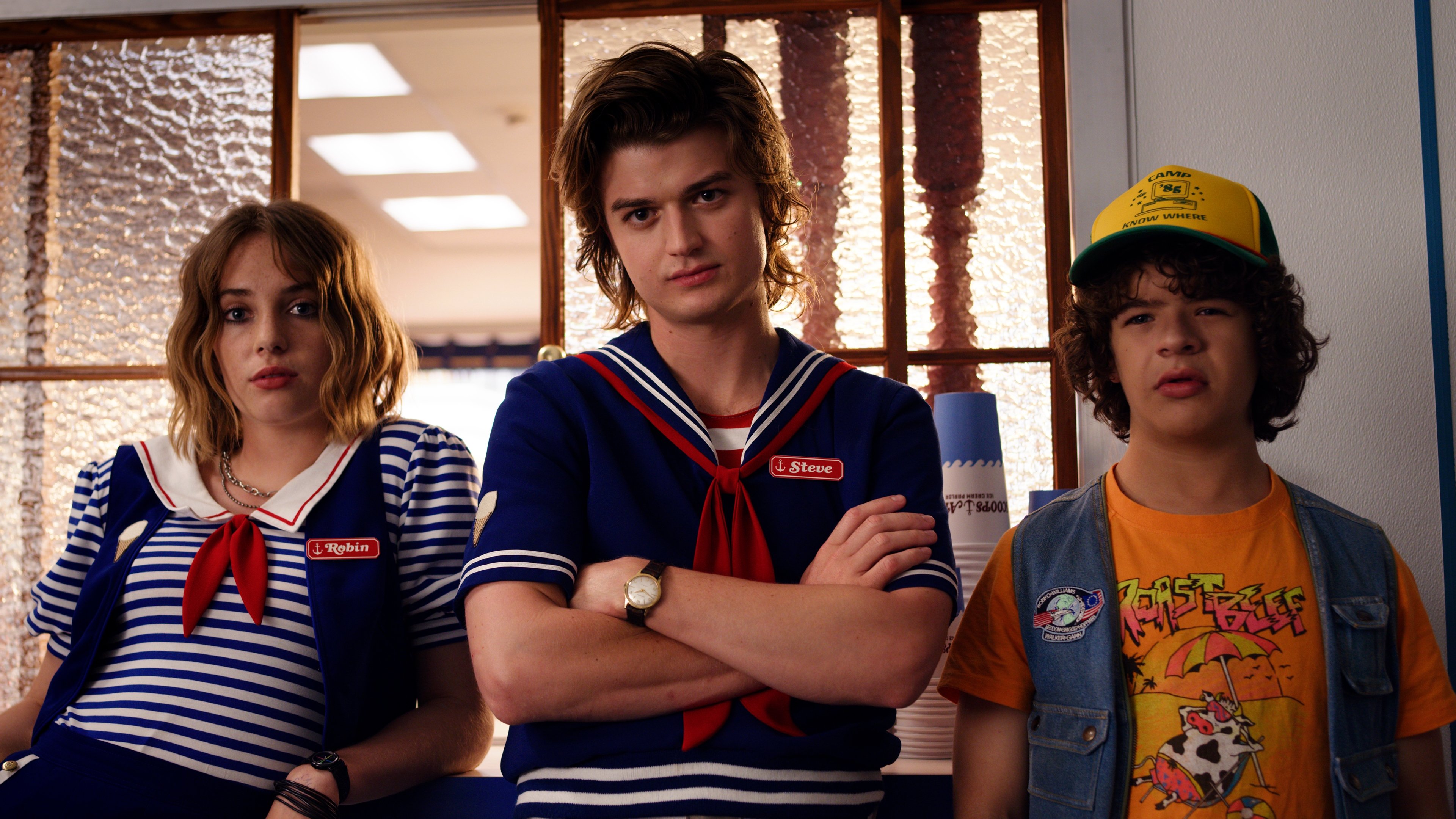 Personagens Robin, Steve e Dustin com uniformes da sorveteria Scoops Ahoy