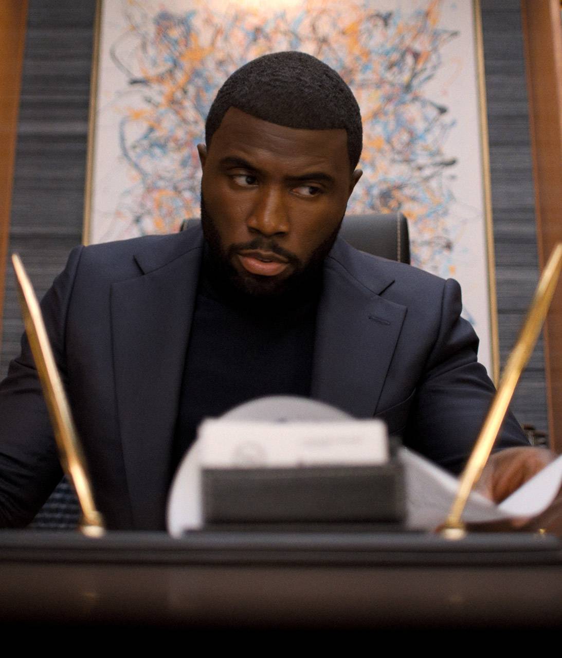 Coltrane de Y'lan Noel olhando pensativo enquanto está sentado em uma mesa em Nemesis