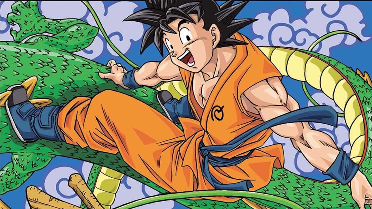 Toyotarou desenhando em mesa de trabalho, com materiais de arte e referência de Dragon Ball ao fundo