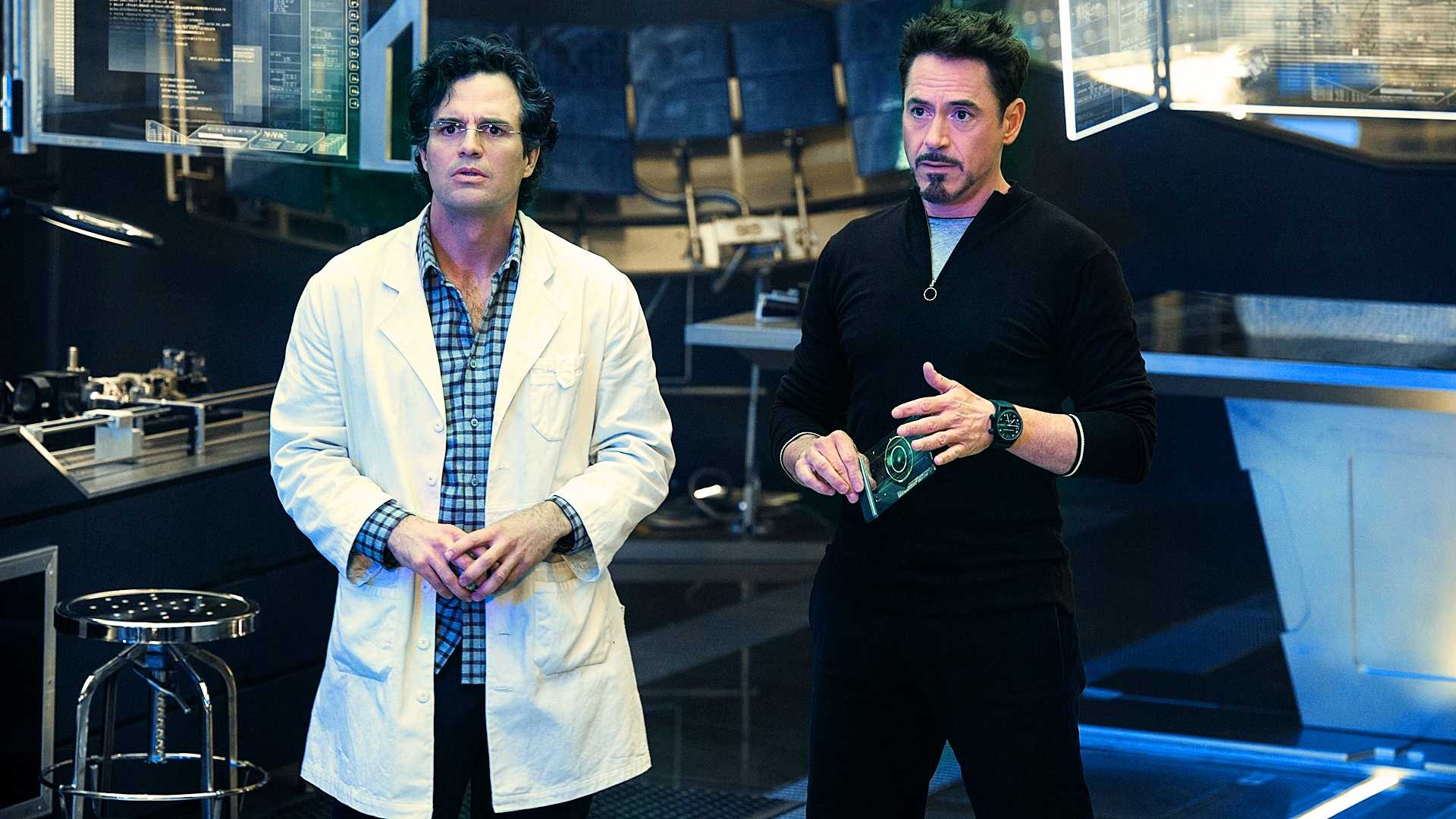 Bruce Banner com jaleco, Tony Stark com roupa escura no laboratório de Avengers Age of Ultron