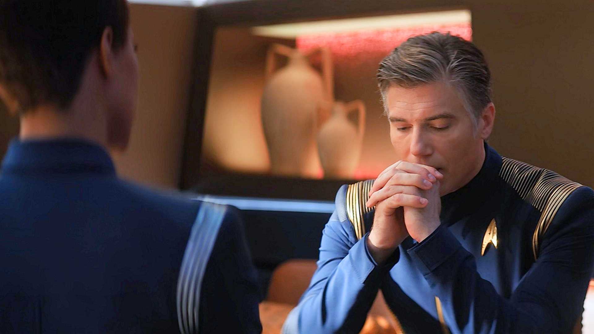 Michael Burnham, de costas para a câmera, encarando o Capitão Pike, olhando para baixo com as mãos unidas perto da boca, na sala de prontidão de Star Trek Discovery
