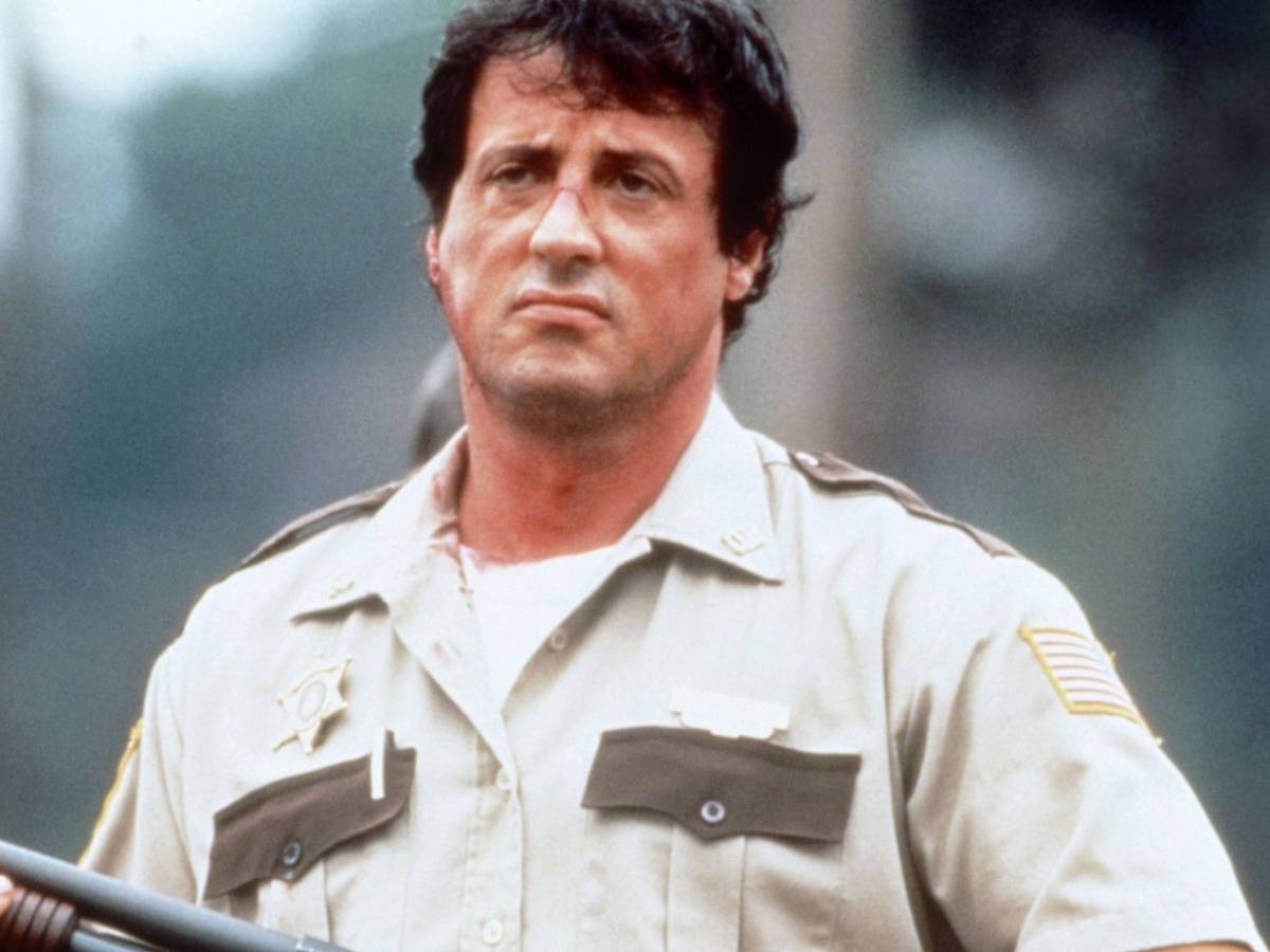 Sylvester Stallone como xerife em Cop Land, cena de rua com policiais ao fundo