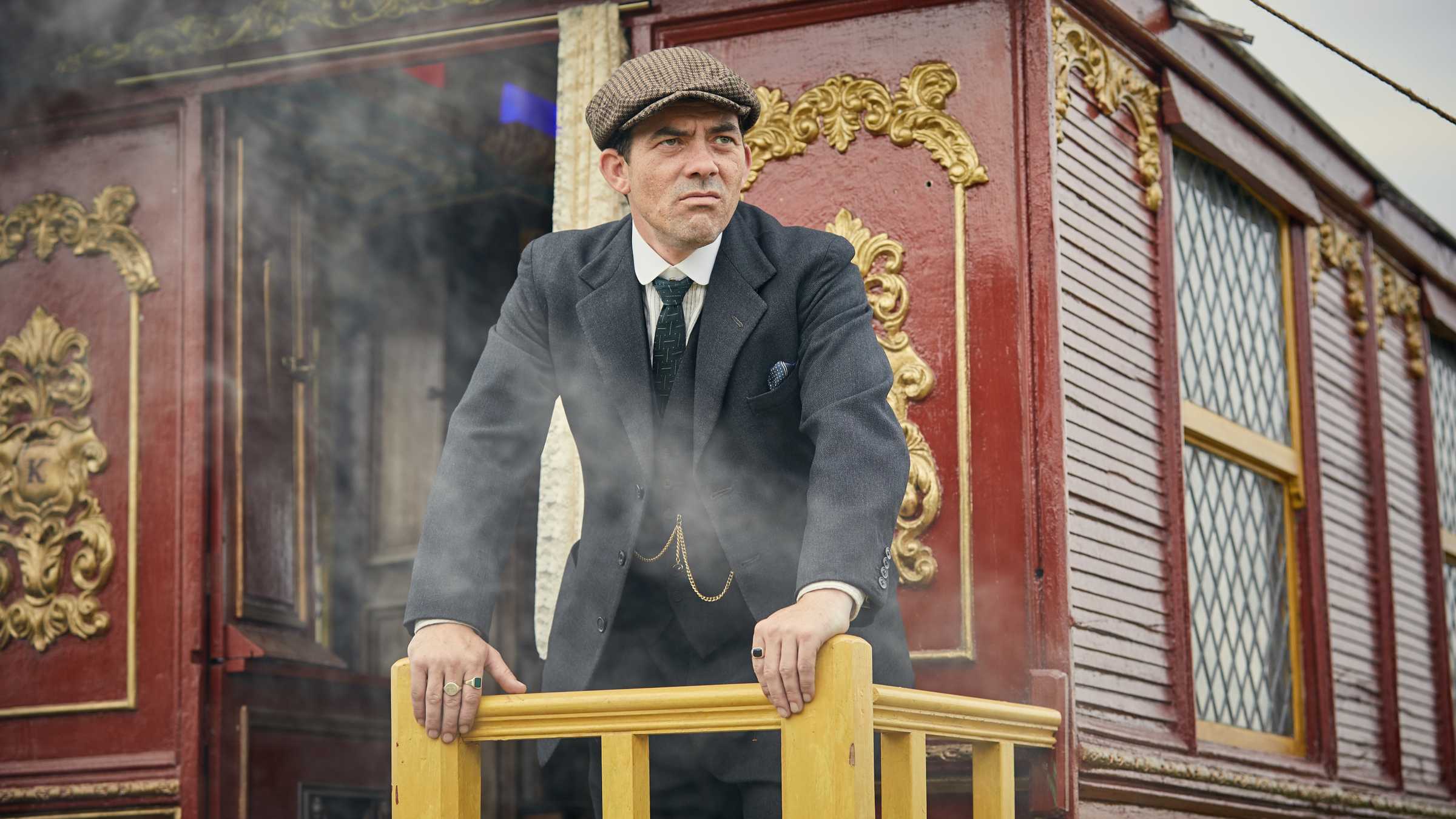 Packy Lee como Johnny Dogs parado fora de uma carruagem e olhando para a distância em Peaky Blinders