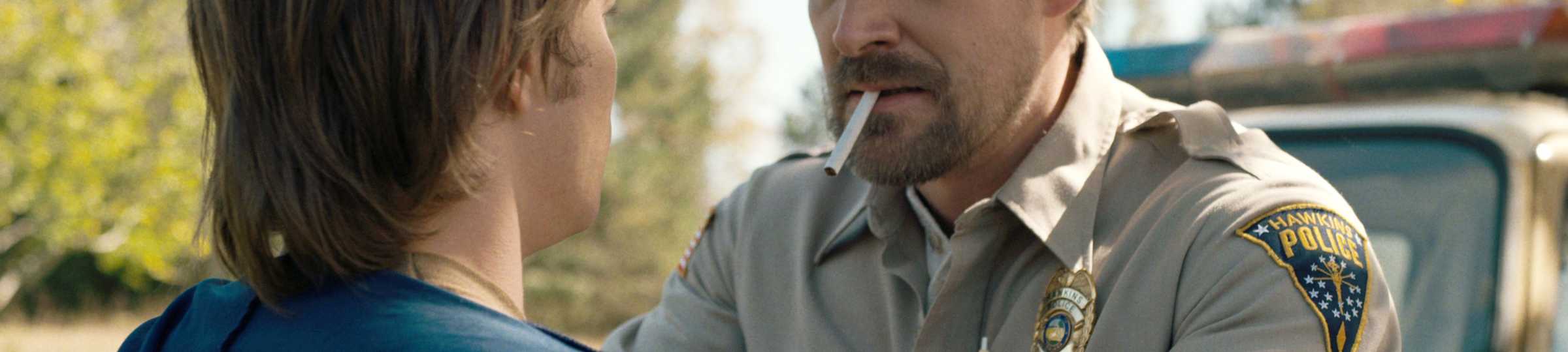 Jim Hopper (David Harbour) segurando os ombros de Jonathan (Charlie Heaton) em Stranger Things temporada 1