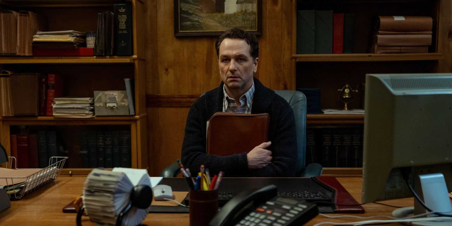 Matthew Rhys como o prefeito Tom Loftis segurando um livro e parecendo nervoso em Widow's Bay.