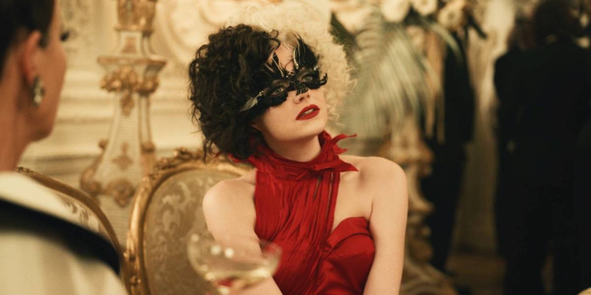 Emma Stone como Cruella de Vil em um vestido vermelho e usando uma máscara em Cruella